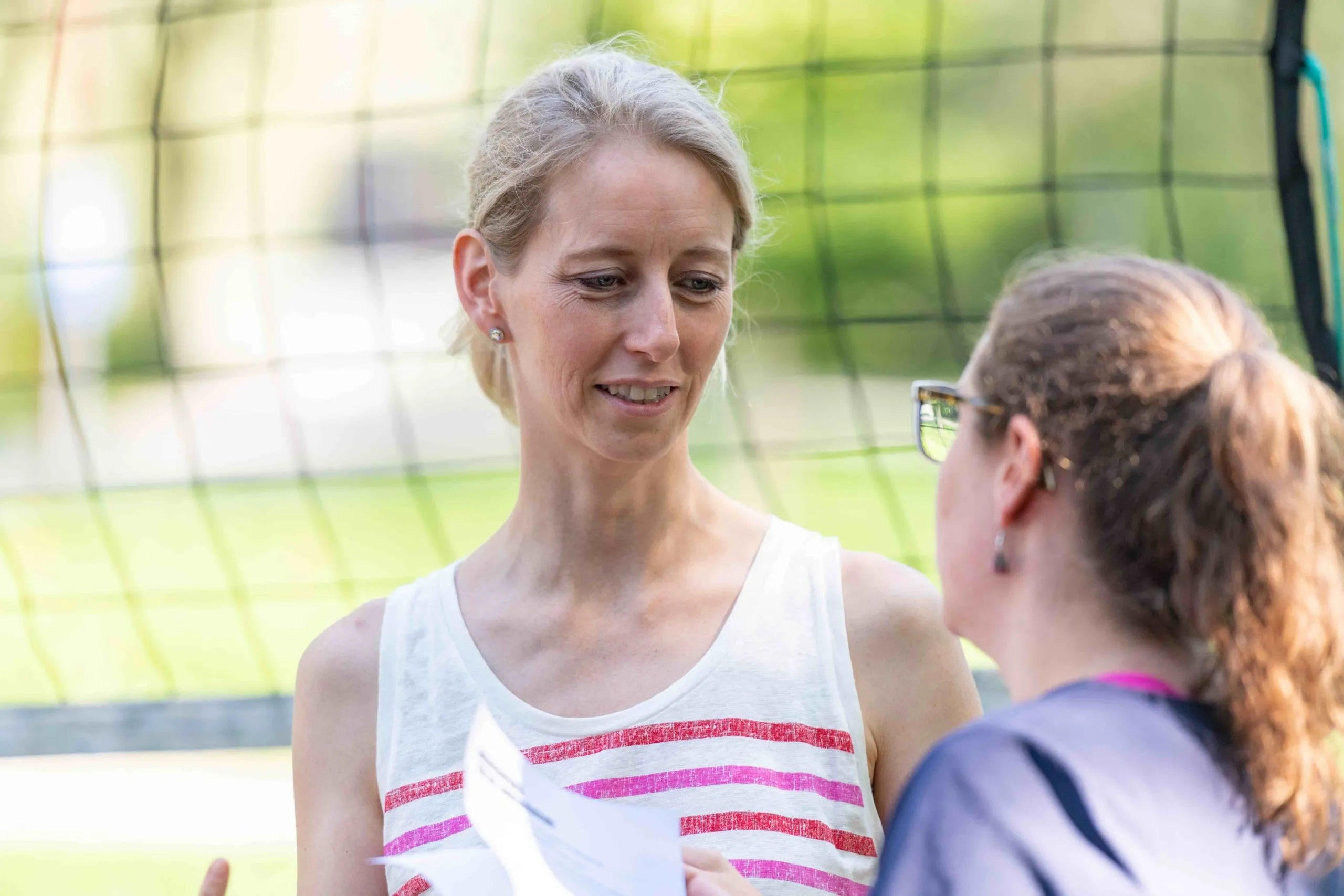 Frau mit blonden Haaren und weißem kurzem T-Shirt unterhält sich mit einer anderen Frau