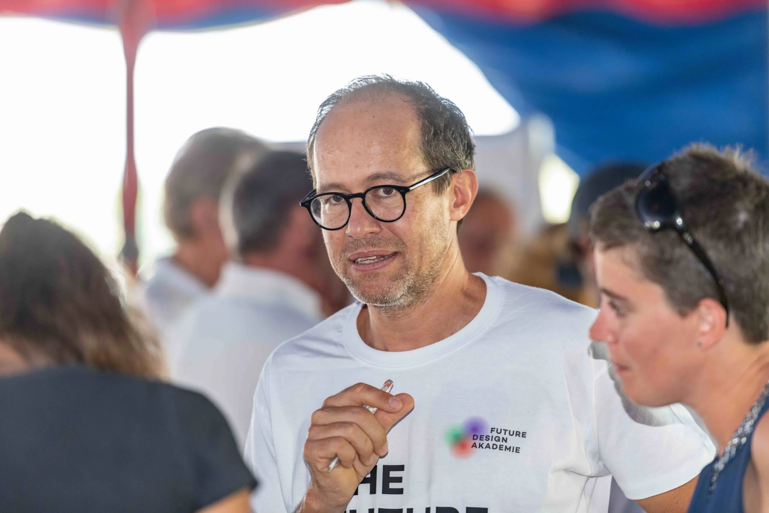 Mann mit Brille und weißem T-Shirt der einen Kugelschreiber in der Hand hält
