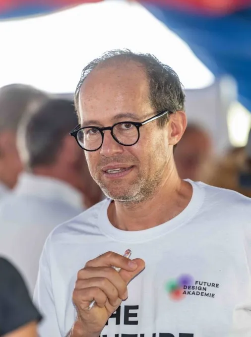 Mann mit Brille und weißem T-Shirt der einen Kugelschreiber in der Hand hält
