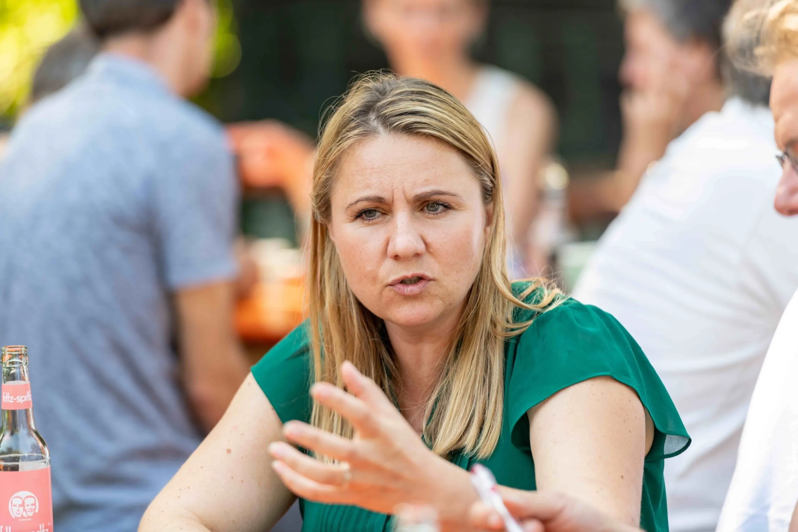 Diskutierende Frau mit langen blonden Haaren und grünem Oberteil