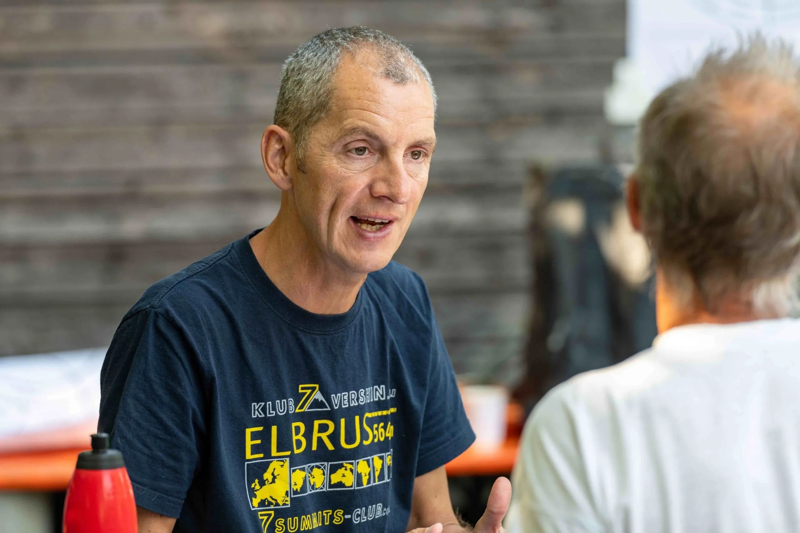 Älterer Mann mit kurzen grauen Haaren und blauem T-Shirt mit gelber Schrift