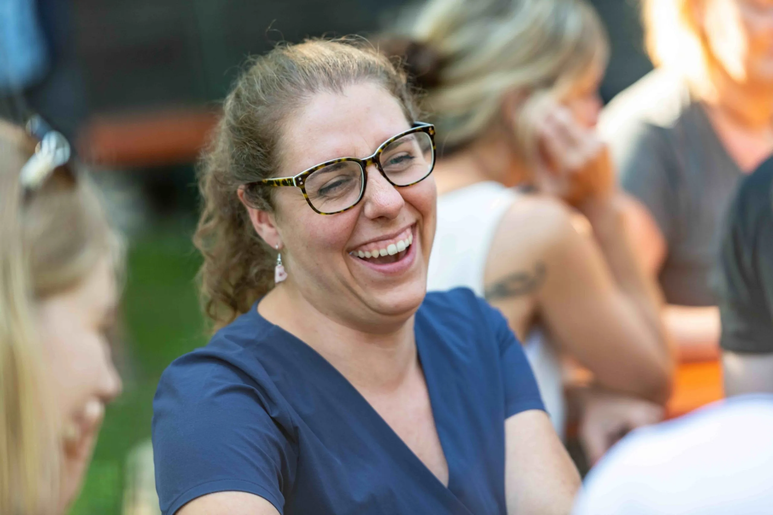 Herzhaft lachende Frau mit Brille und blauem Oberteil