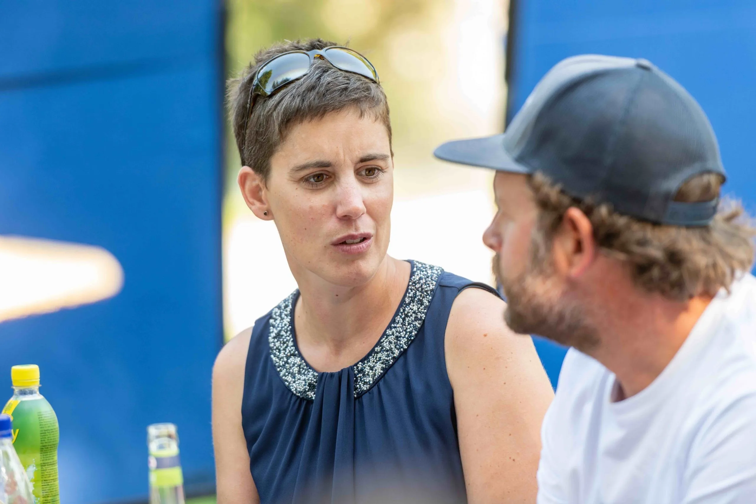 Eine Frau mit kurzen Haaren und blauem Oberteil unterhält sich mit einem Mann in blauem Baseballcap