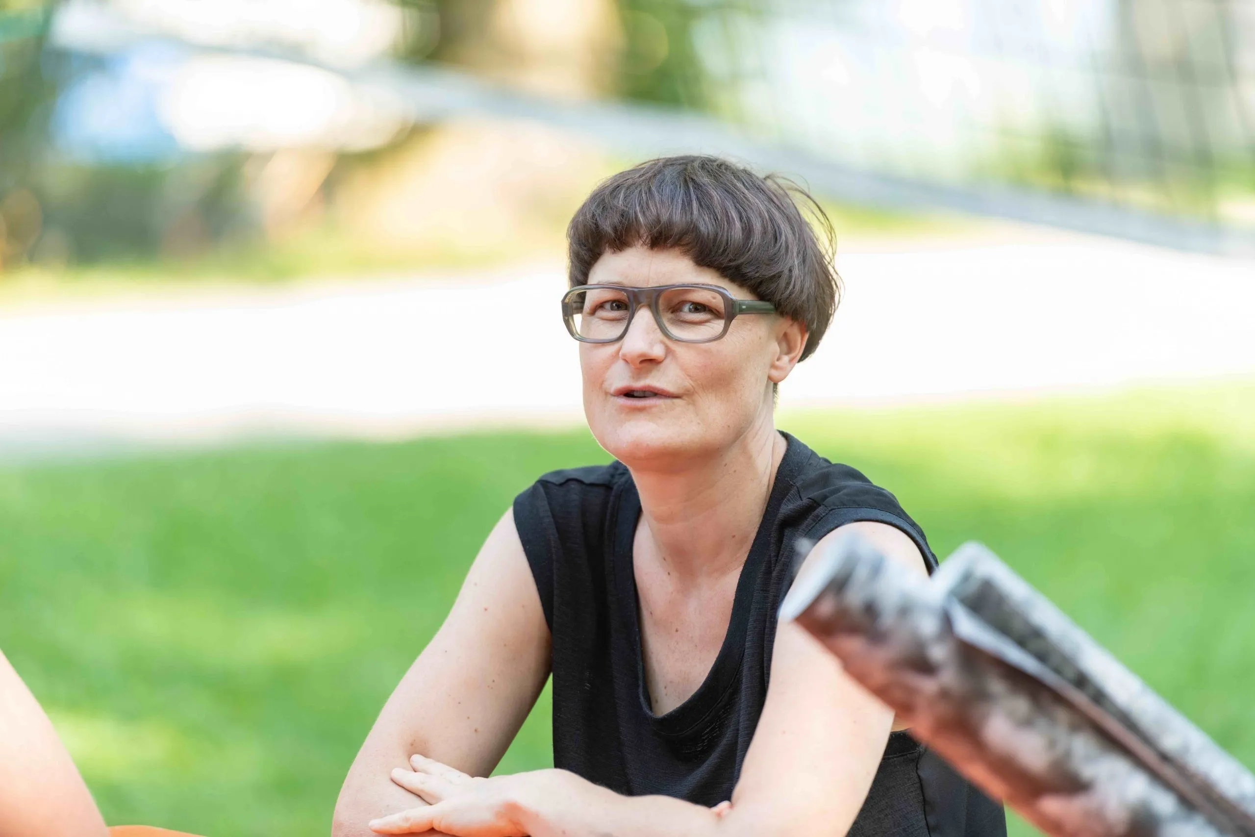 Frau mit kurzen braunen Haaren, grüner Brille und schwarzem Oberteil