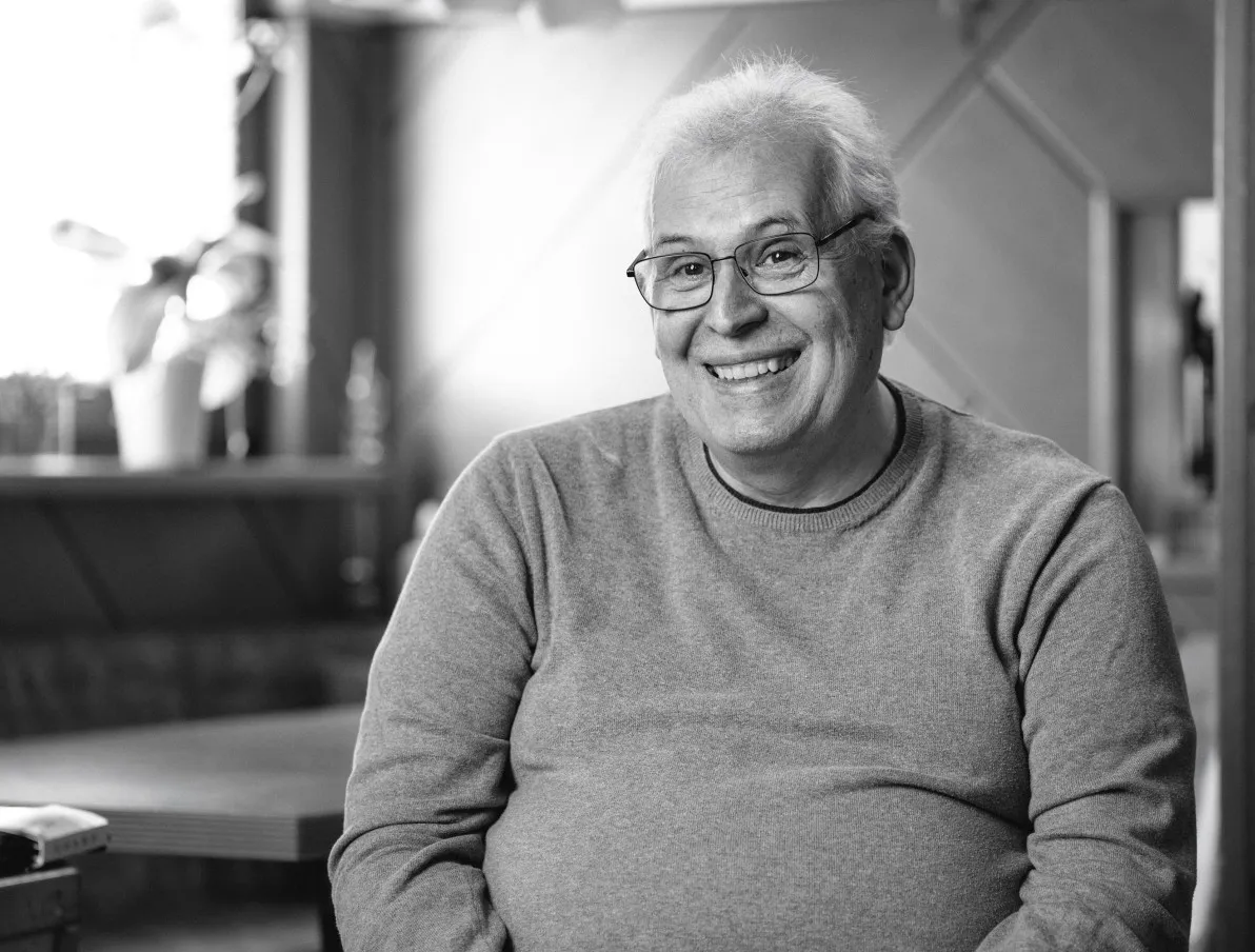 Lächelnder älterer Mann mit Brille in grauem Pullover, Schwarz-Weiß-Porträt.